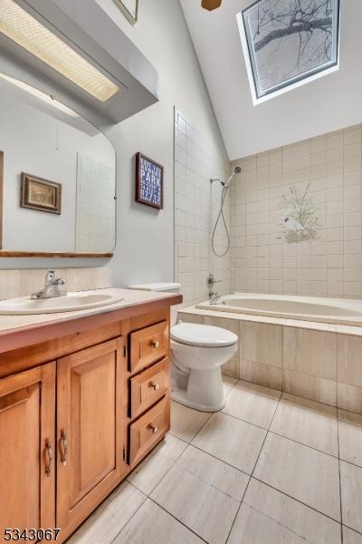 full bath featuring vanity, vaulted ceiling with skylight, tiled shower / bath combo, tile patterned floors, and toilet