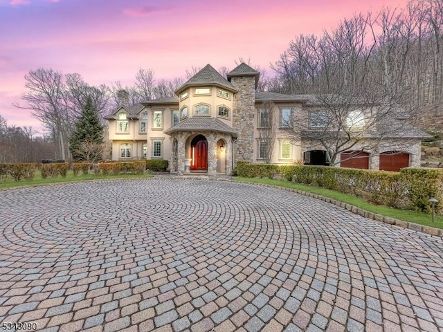 view of front of house with stucco siding, decorative driveway, a high end roof, stone siding, and a chimney