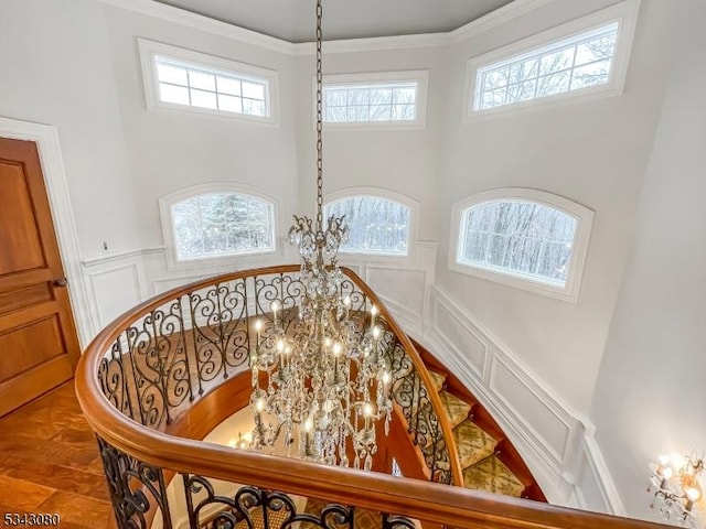 stairway featuring a towering ceiling, a healthy amount of sunlight, an inviting chandelier, and ornamental molding