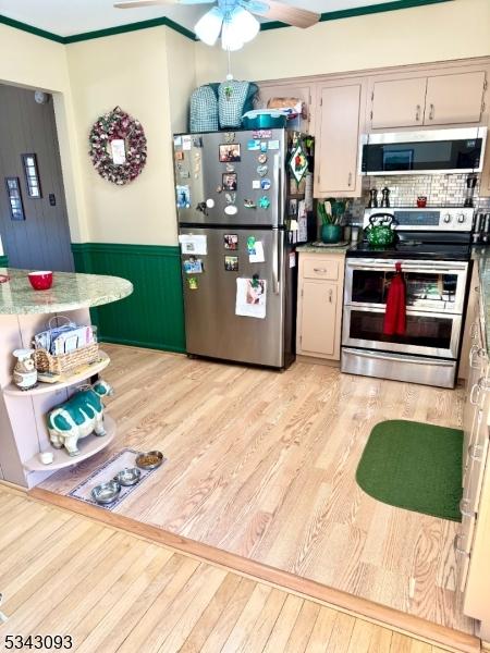 kitchen with light wood-type flooring, ornamental molding, a ceiling fan, backsplash, and stainless steel appliances