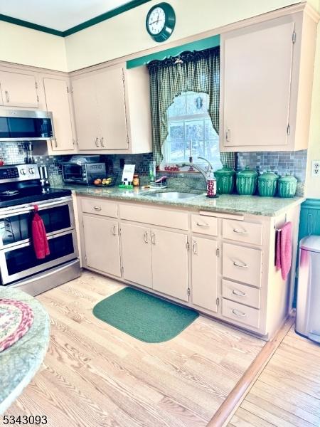 kitchen with backsplash, light countertops, appliances with stainless steel finishes, light wood-style floors, and a sink