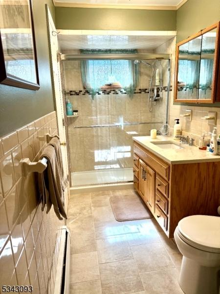 bathroom with vanity, a stall shower, tile walls, toilet, and baseboard heating