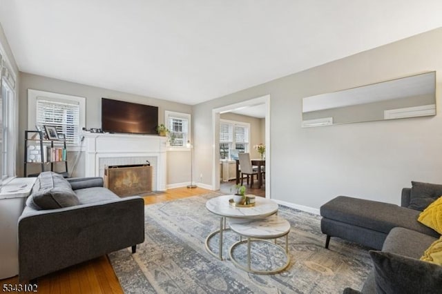 living area with wood finished floors, baseboards, a wealth of natural light, and a tile fireplace