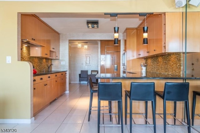 kitchen featuring built in refrigerator, backsplash, dark countertops, a peninsula, and light tile patterned flooring