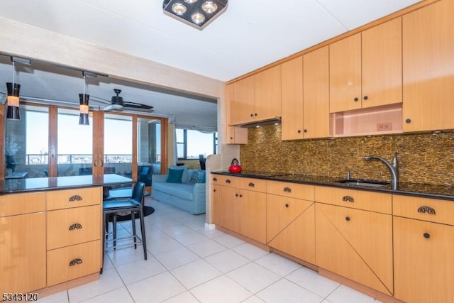 kitchen with light brown cabinetry, a sink, under cabinet range hood, dark stone countertops, and backsplash