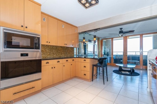 kitchen featuring stainless steel oven, built in microwave, backsplash, and light brown cabinetry