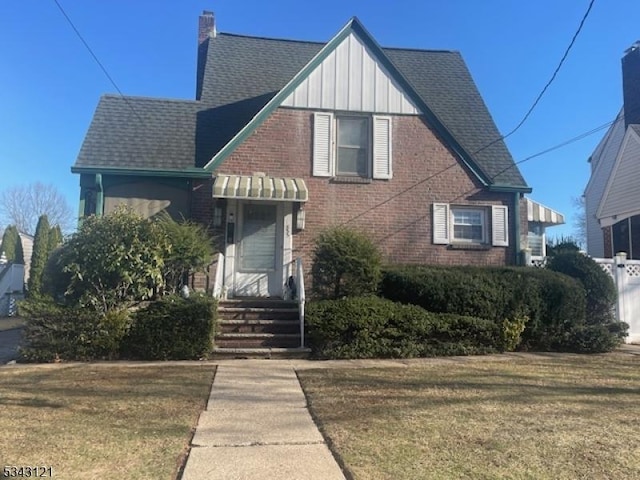 view of front of home featuring brick siding, a front lawn, a chimney, and roof with shingles