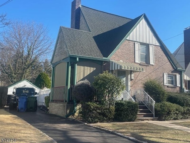 view of front of home with an outbuilding, driveway, a shingled roof, brick siding, and a chimney