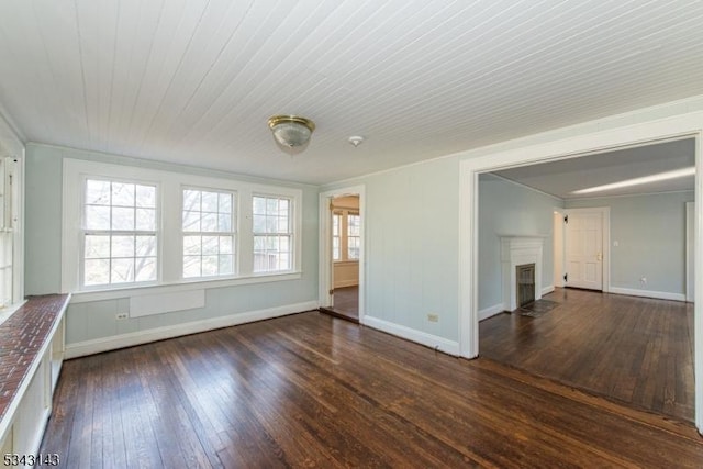 spare room with baseboards, a fireplace with flush hearth, a healthy amount of sunlight, and hardwood / wood-style flooring