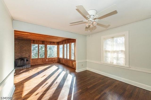 unfurnished living room with a ceiling fan, a wood stove, plenty of natural light, and wood finished floors