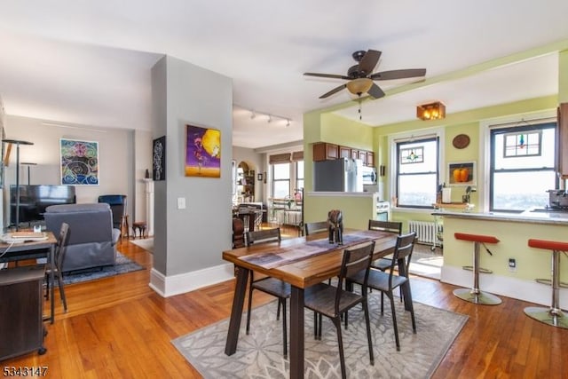 dining room with radiator, a ceiling fan, baseboards, track lighting, and wood-type flooring