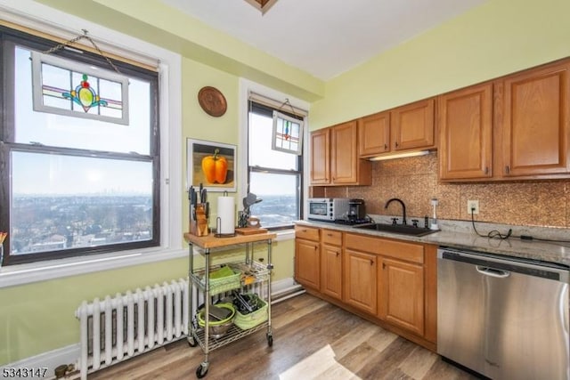 kitchen featuring light wood-type flooring, radiator heating unit, decorative backsplash, stainless steel dishwasher, and a sink