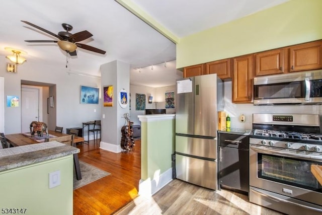 kitchen with brown cabinetry, track lighting, light wood-style floors, appliances with stainless steel finishes, and tasteful backsplash