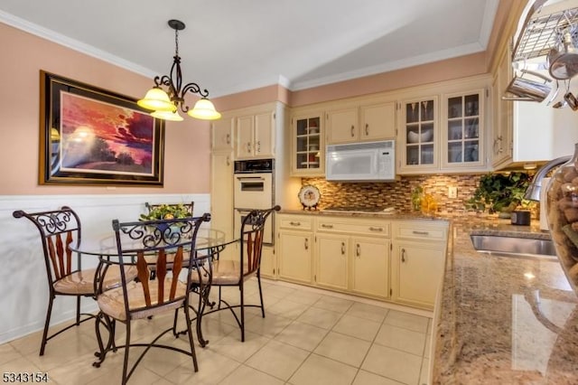 kitchen with pendant lighting, a sink, cream cabinets, white appliances, and crown molding