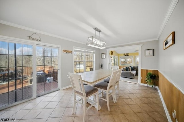 dining room with crown molding, wooden walls, light tile patterned floors, and a wainscoted wall