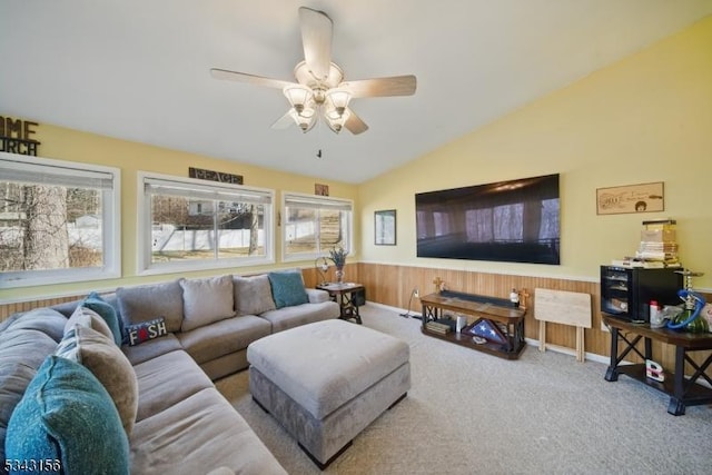 carpeted living area with wooden walls, wainscoting, a ceiling fan, and vaulted ceiling