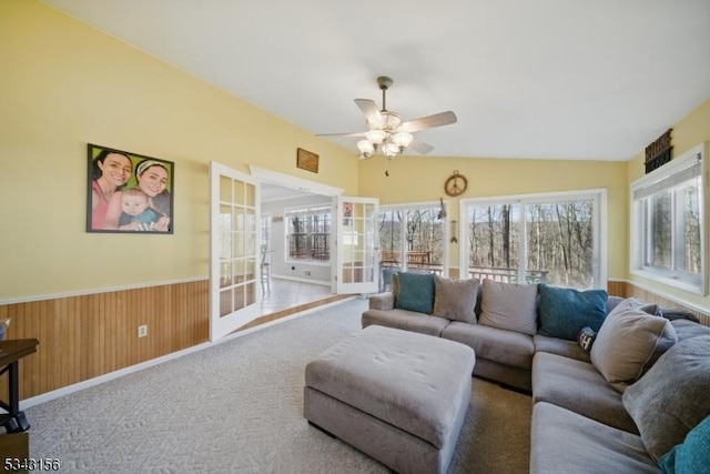 living area with ceiling fan, a wainscoted wall, wood walls, lofted ceiling, and carpet flooring