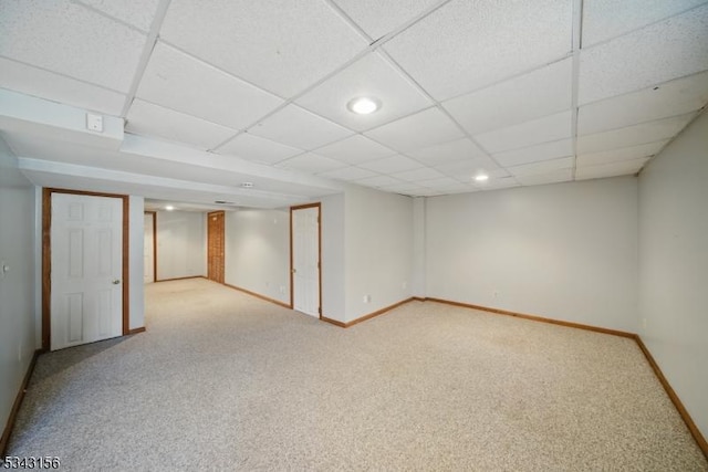 finished below grade area featuring a drop ceiling, baseboards, and carpet floors