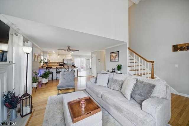 living room featuring baseboards, light wood-style flooring, ceiling fan, stairs, and crown molding