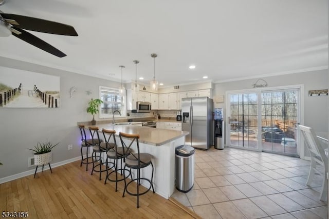 kitchen featuring a kitchen bar, a peninsula, crown molding, and appliances with stainless steel finishes