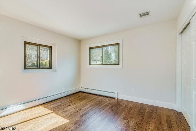 spare room featuring visible vents, wood finished floors, baseboards, and a baseboard radiator