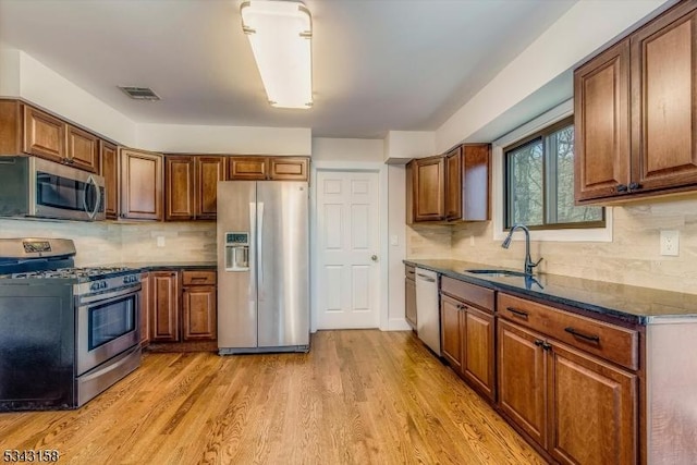 kitchen with light wood finished floors, visible vents, appliances with stainless steel finishes, brown cabinetry, and a sink