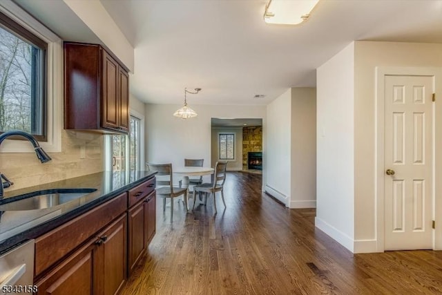 kitchen with a sink, tasteful backsplash, a stone fireplace, and dark wood-style flooring