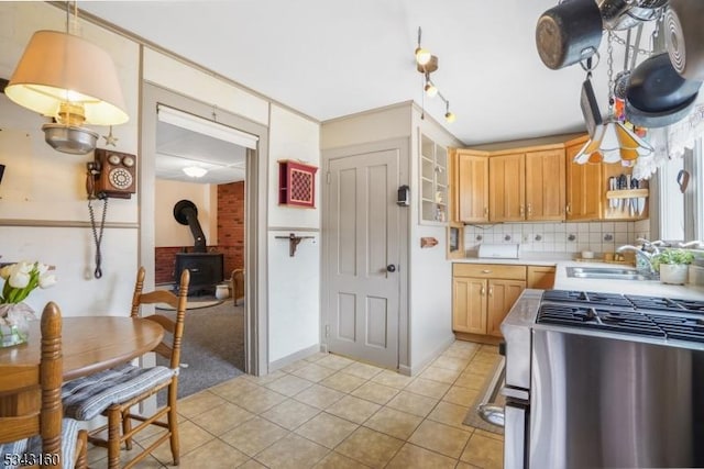 kitchen featuring backsplash, light countertops, a wood stove, stainless steel gas range, and a sink