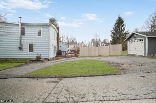 view of yard with fence, aphalt driveway, a deck, a garage, and an outbuilding