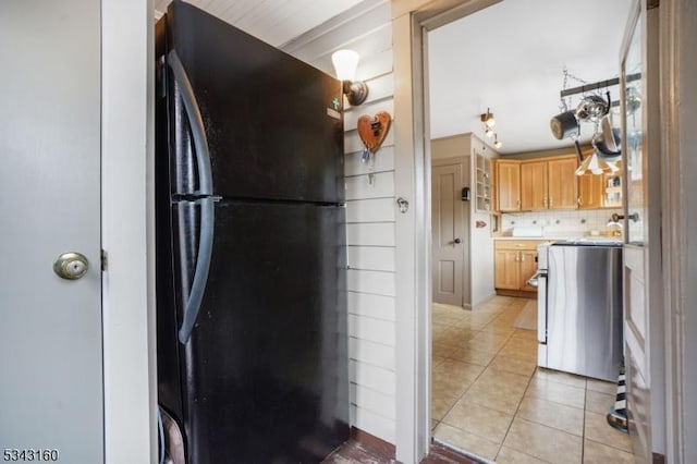 kitchen with light tile patterned flooring, freestanding refrigerator, light countertops, range, and backsplash