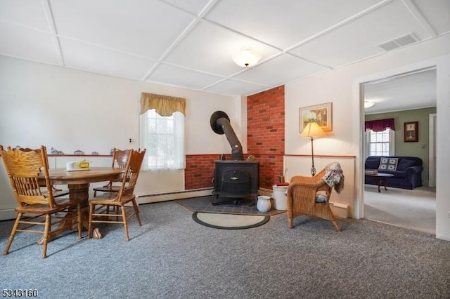 carpeted dining room featuring a baseboard heating unit, a wood stove, a paneled ceiling, and visible vents