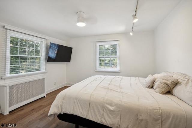 bedroom with a ceiling fan, track lighting, wood finished floors, radiator heating unit, and baseboards