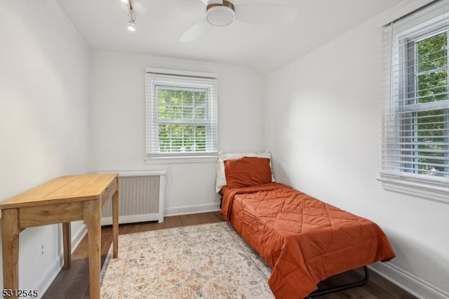 bedroom with radiator, ceiling fan, baseboards, rail lighting, and wood finished floors