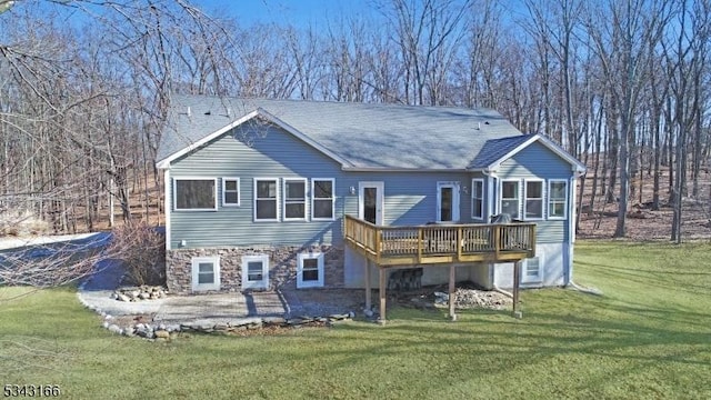 back of property featuring a patio, a shingled roof, stone siding, a deck, and a lawn