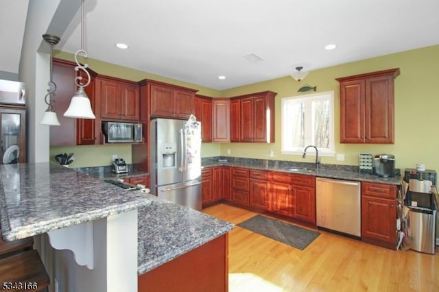 kitchen with a peninsula, a sink, stainless steel appliances, light wood-style floors, and decorative light fixtures