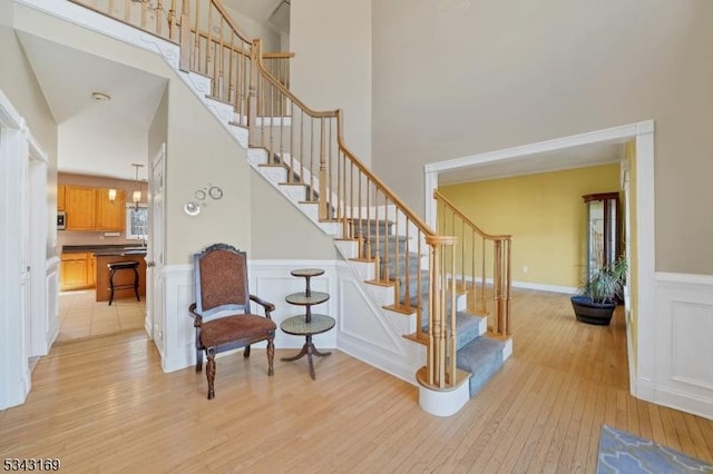 staircase featuring a high ceiling, a decorative wall, wood finished floors, and a wainscoted wall