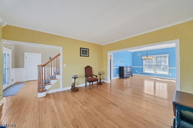 living area with stairs, a notable chandelier, light wood finished floors, and ornamental molding