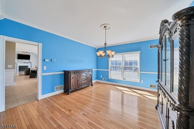 unfurnished room with crown molding, a notable chandelier, visible vents, and light wood finished floors