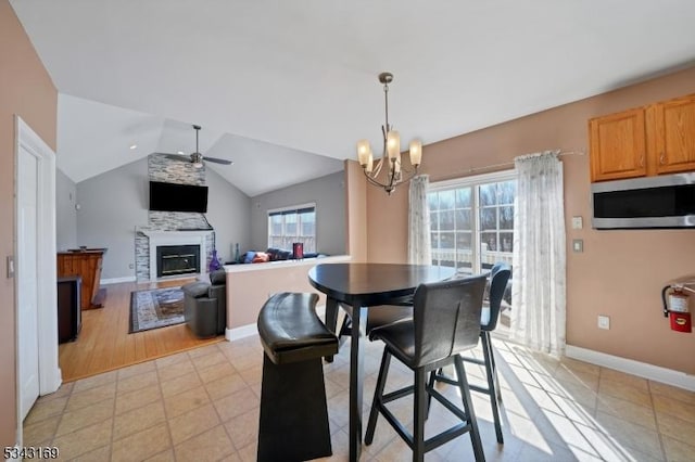 dining room with plenty of natural light, ceiling fan with notable chandelier, lofted ceiling, and a glass covered fireplace