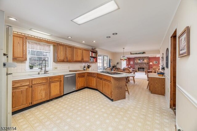 kitchen featuring brown cabinetry, a peninsula, a sink, stainless steel dishwasher, and open floor plan