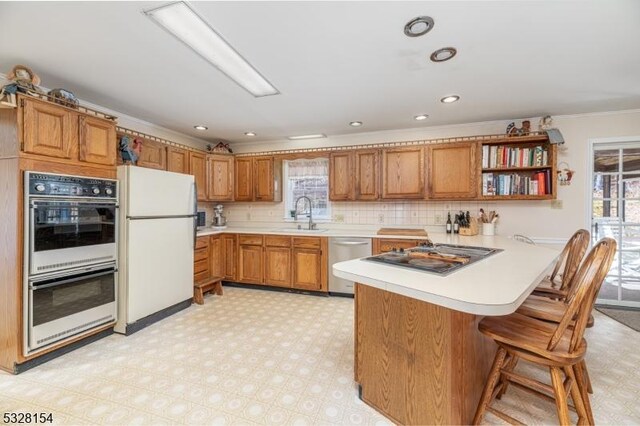 kitchen with open shelves, appliances with stainless steel finishes, a peninsula, brown cabinetry, and light countertops