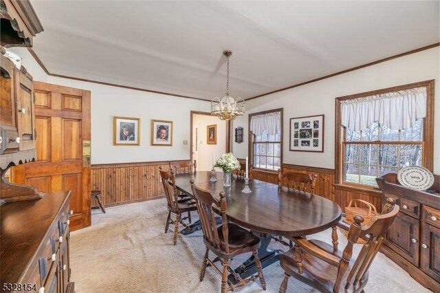 dining room with a notable chandelier, wainscoting, light colored carpet, and ornamental molding