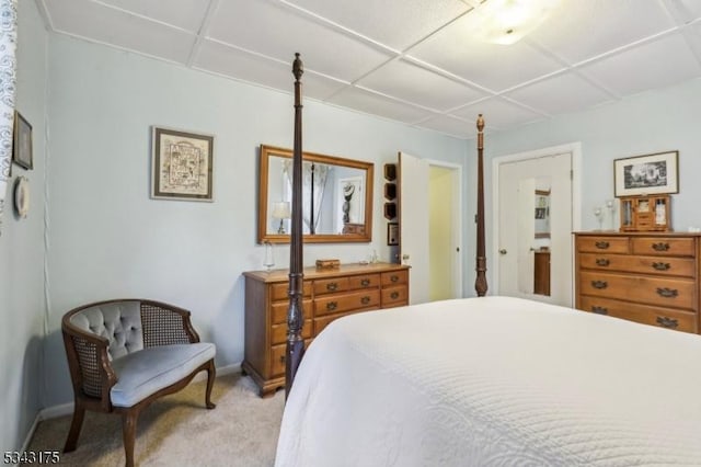 bedroom featuring light carpet, a drop ceiling, and baseboards