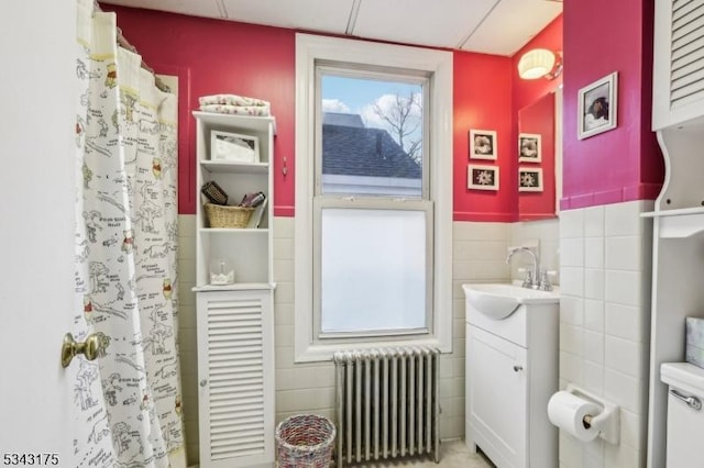 full bathroom featuring curtained shower, tile walls, a wainscoted wall, radiator heating unit, and vanity