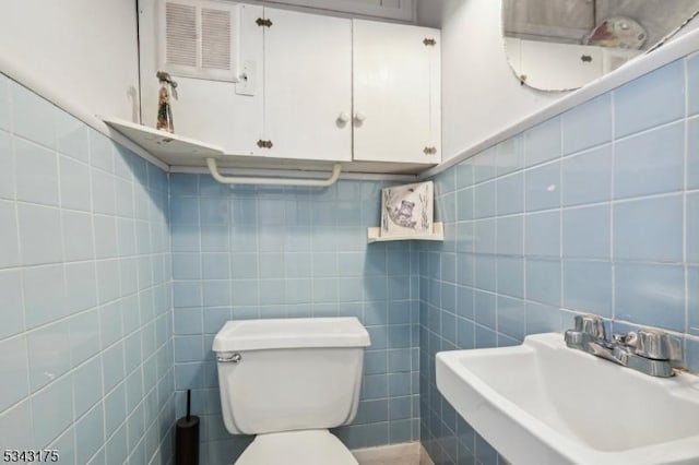 half bath with a sink, toilet, and tile walls