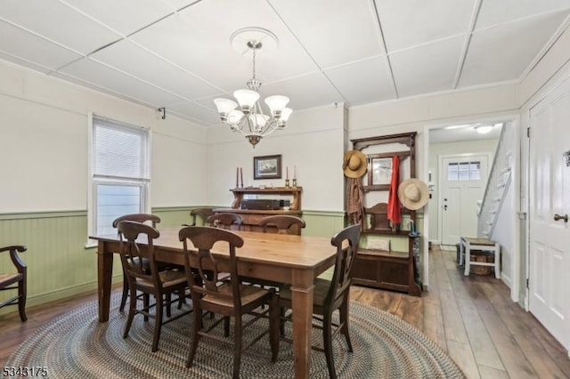 dining room with an inviting chandelier, wood finished floors, a wainscoted wall, and a healthy amount of sunlight