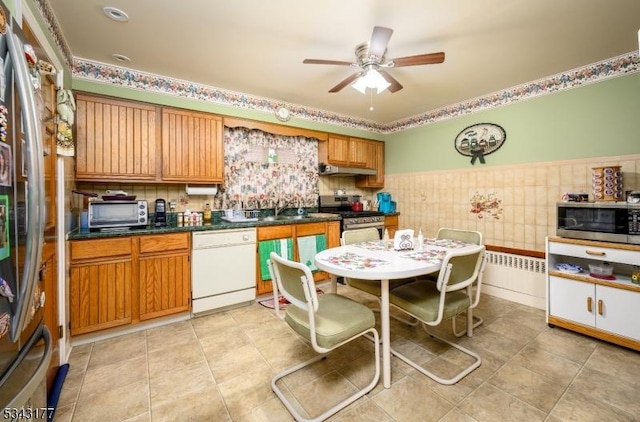 kitchen with under cabinet range hood, dark countertops, stainless steel appliances, light tile patterned floors, and ceiling fan