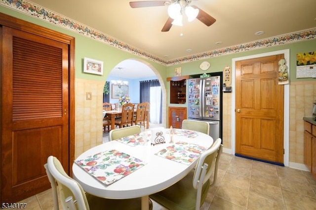 dining room featuring arched walkways, ceiling fan with notable chandelier, tile walls, and light tile patterned flooring