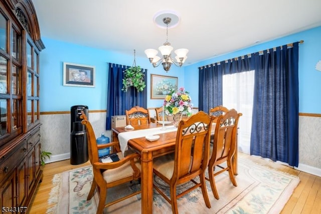 dining area with light wood-type flooring, wainscoting, and a chandelier