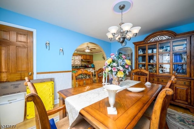 dining area with an inviting chandelier, arched walkways, light wood finished floors, and wainscoting